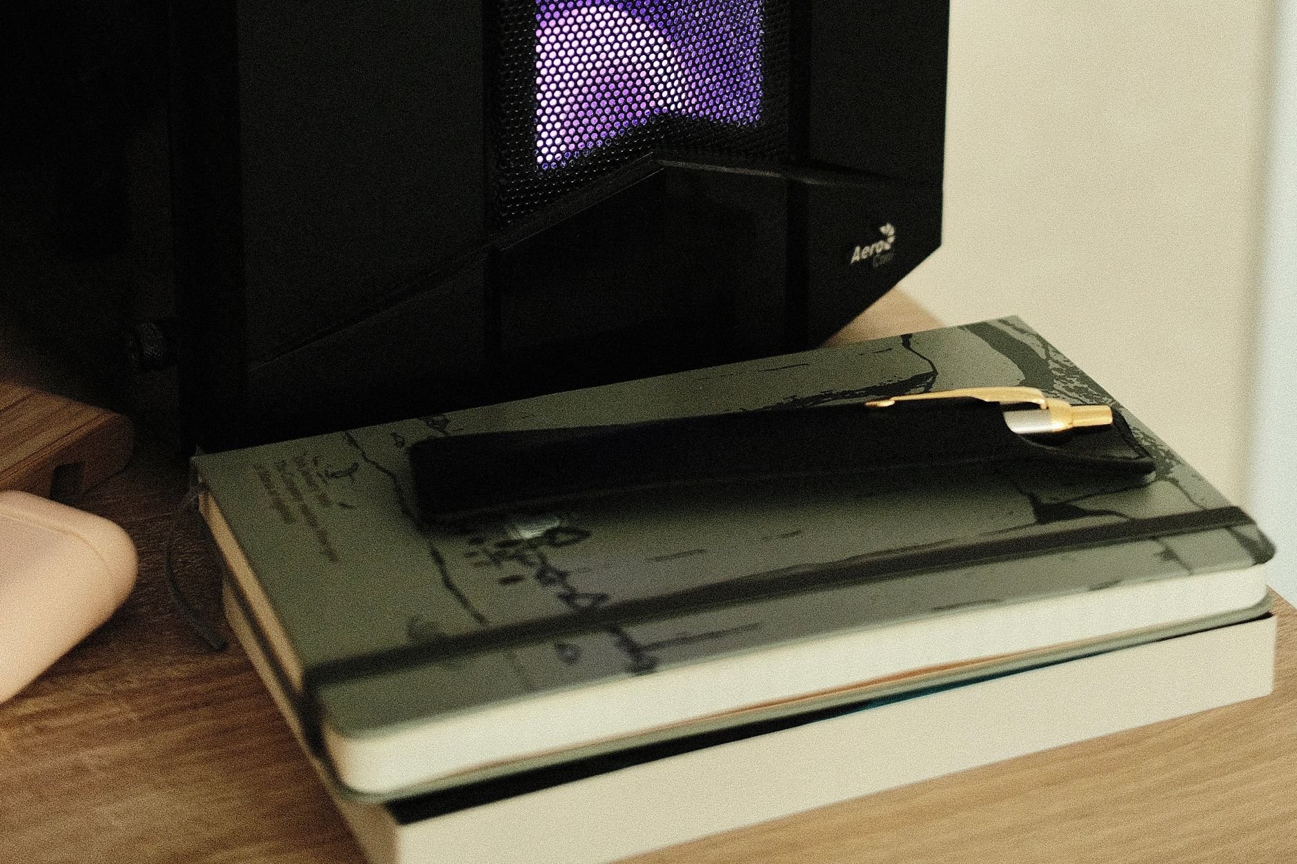 A cozy desk setup featuring a stack of notebooks, a pen, and a warm desk lamp glow.