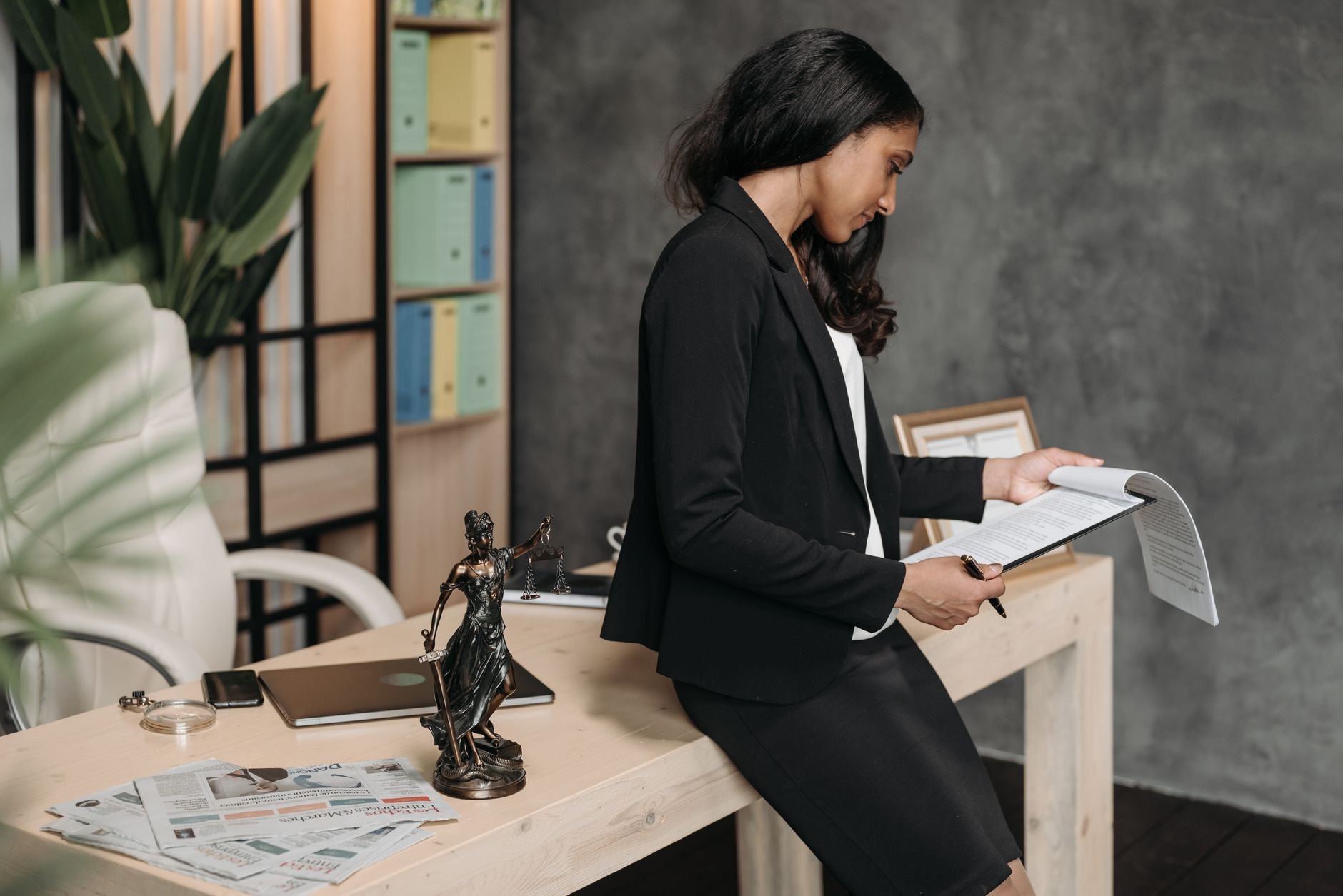 A professional woman in a business suit reviews legal documents at her office desk.